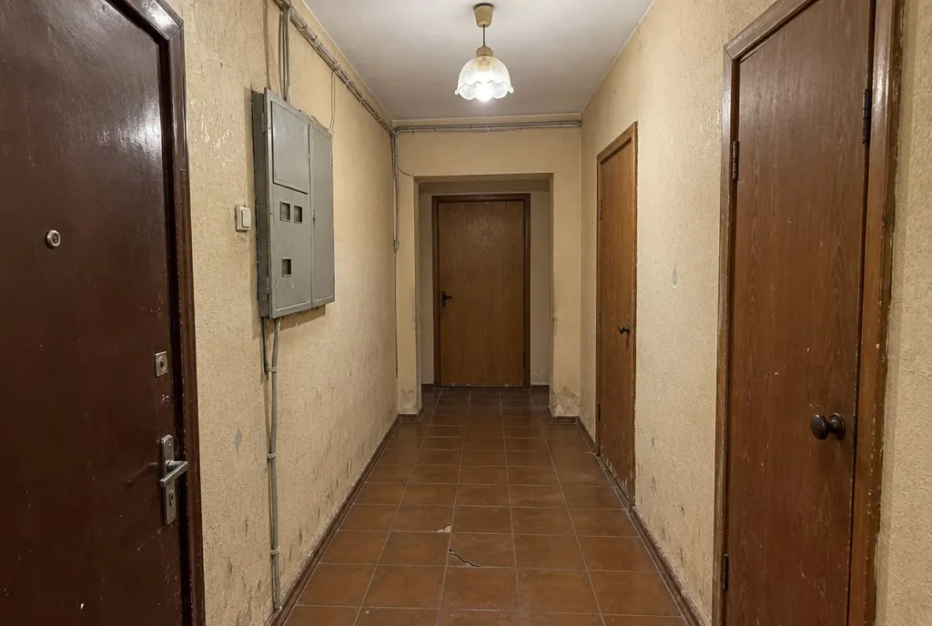 Le même couloir avant travaux : enduit taché, carrelage ancien fissuré, tableau électrique et câbles apparents