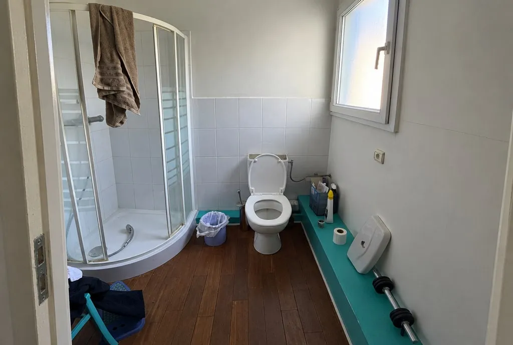 La même salle de bain avant travaux : cabine de douche d'angle, WC au sol, coffrage turquoise